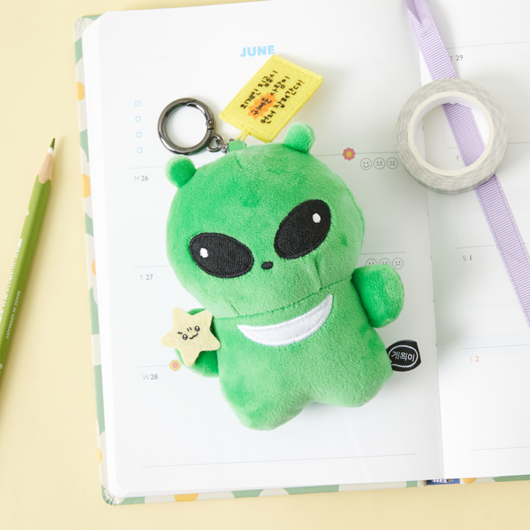 Official Artbox photograph of a green Gwaeki alien plush mini keyring on a notebook.